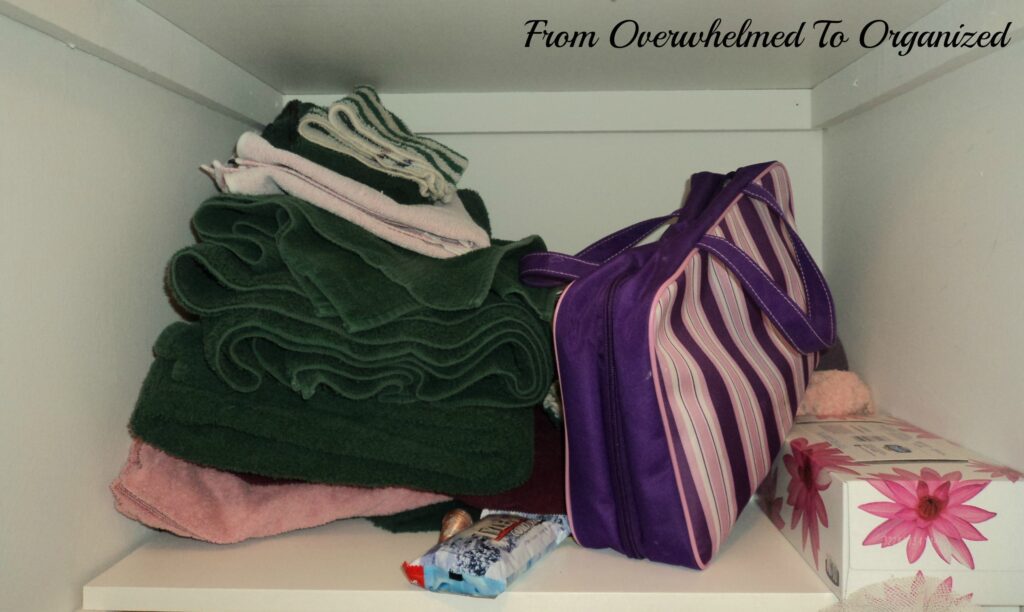 Linen closet before organization. Towels, tissues and makeup bag on shelf. 