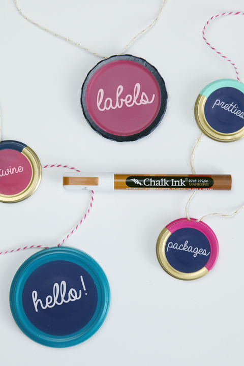 Painted jar lids used as labels. Chalk ink pen used to write on top of jar lids. Edges of lids have been painted blues, pink and gold.
