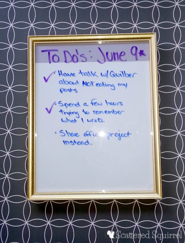 DIY whiteboard made with gold art frame with white paper behind glass. A to-do list is printed in purple and blue ink.