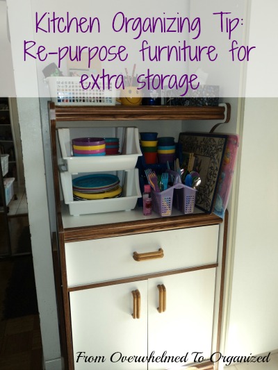 Kitchen organizing tip. Re-purpose furniture for extra storage. Microwave cart with a drawer and bottom cupboard tucked into corner used to store colourful plastic dishes. White stackable bins a mauve cutlery caddy and other containers hold various kitchen tools. From overwhelmed to organized.
