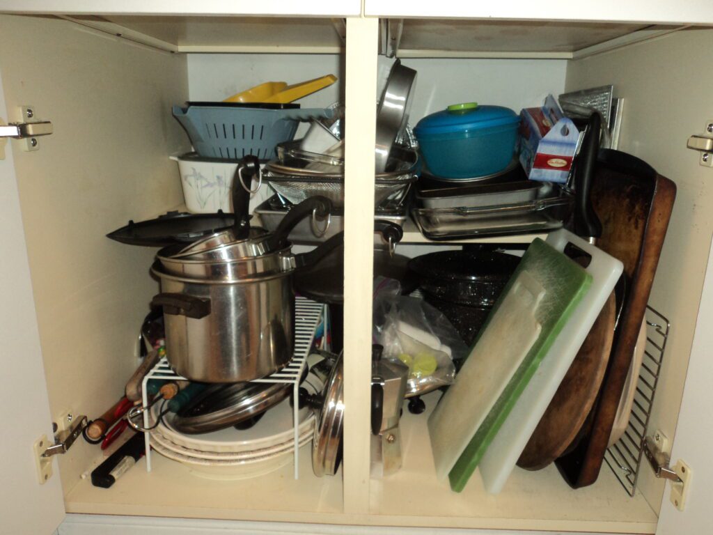 Cluttered kitchen cabinet with pots and pans before organization.