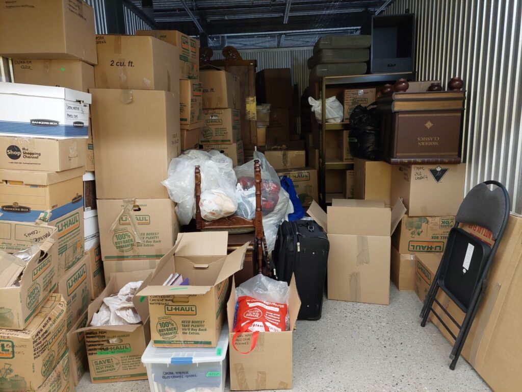 Large storage unit nearly full of cardboard boxes and small furniture. 